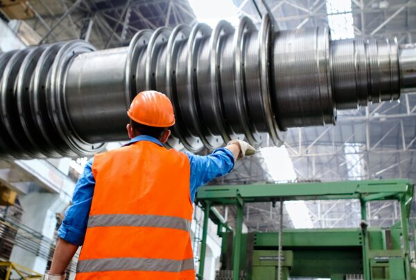 Industrial millwright inspecting a heavy machined shaft during equipment installation in a manufacturing facility