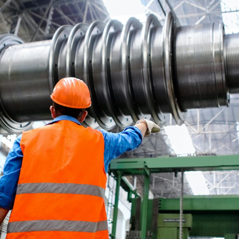Industrial millwright inspecting a heavy machined shaft during equipment installation in a manufacturing facility